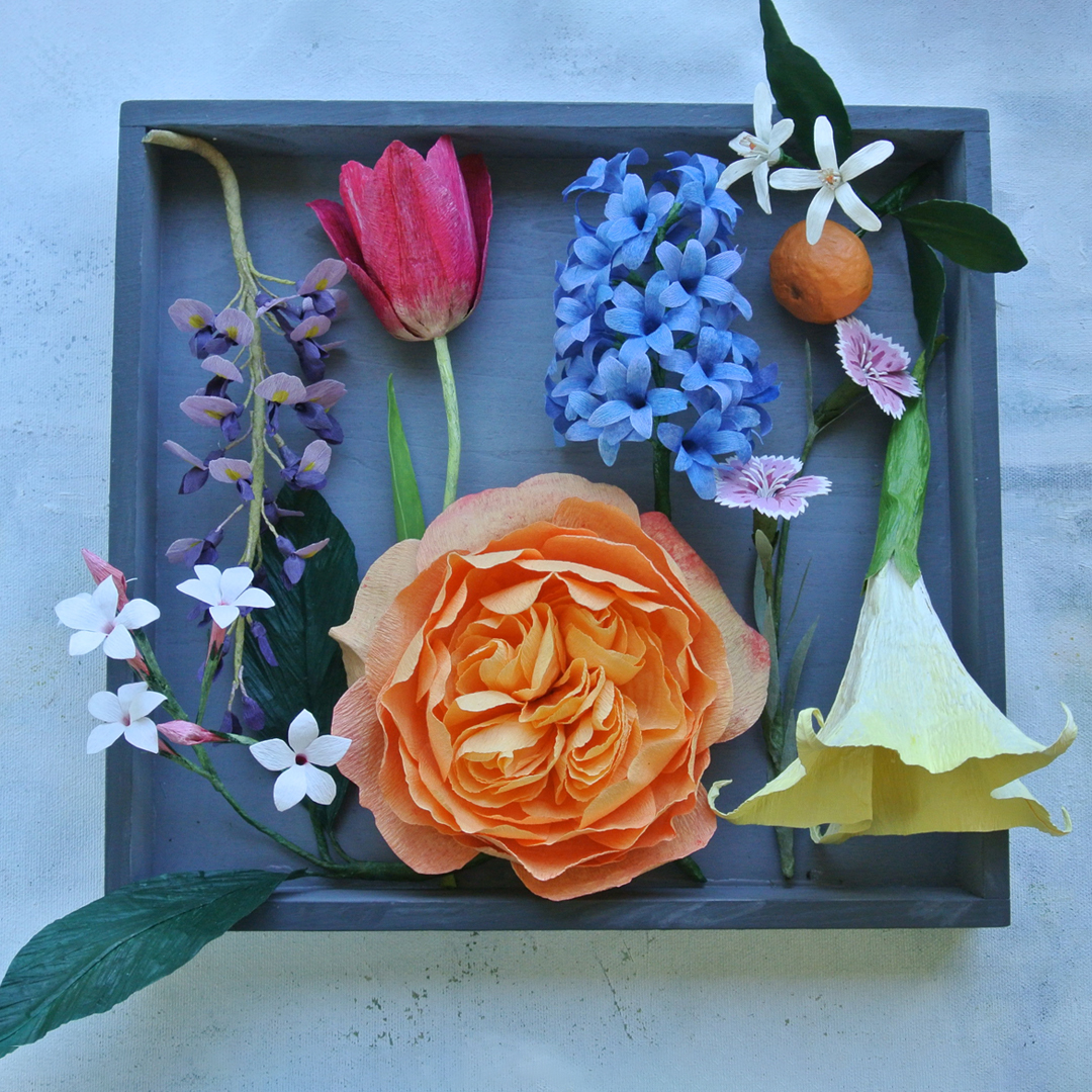 Multi coloured handmade flowers organised neatly  in a grey shallow box